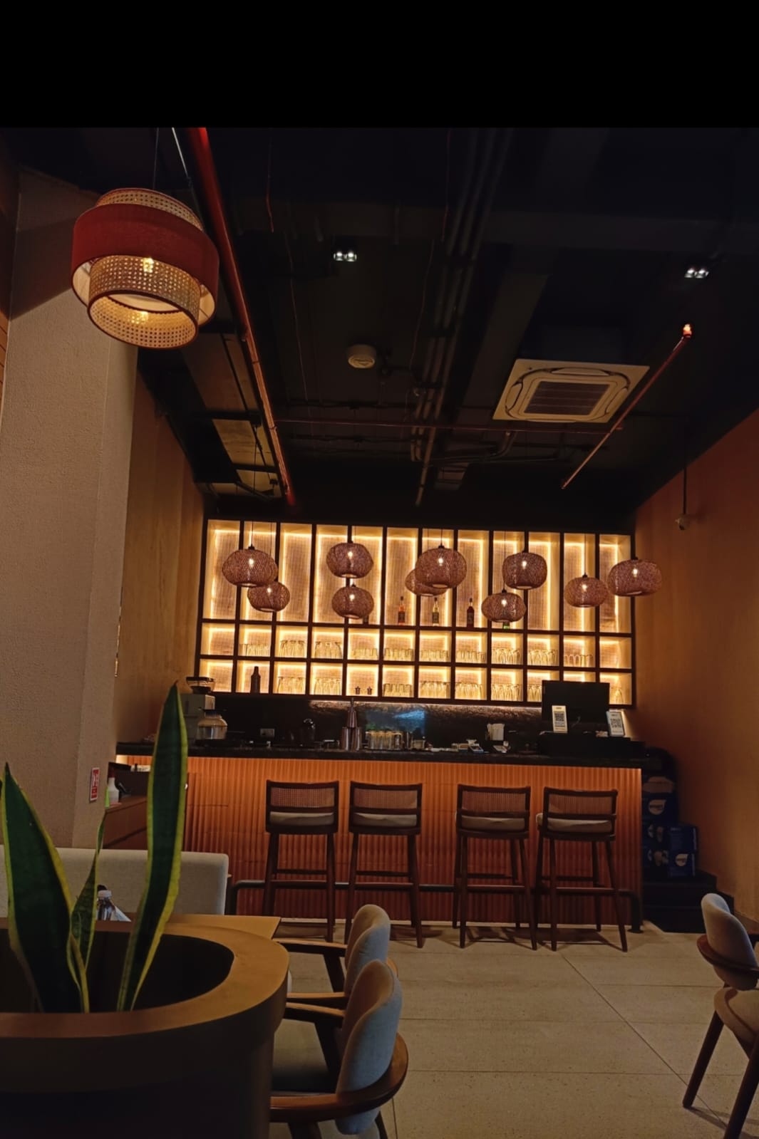 The image is of a cafe and shows a bar with lamps on top hanging from the ceiling and 4 chairs.